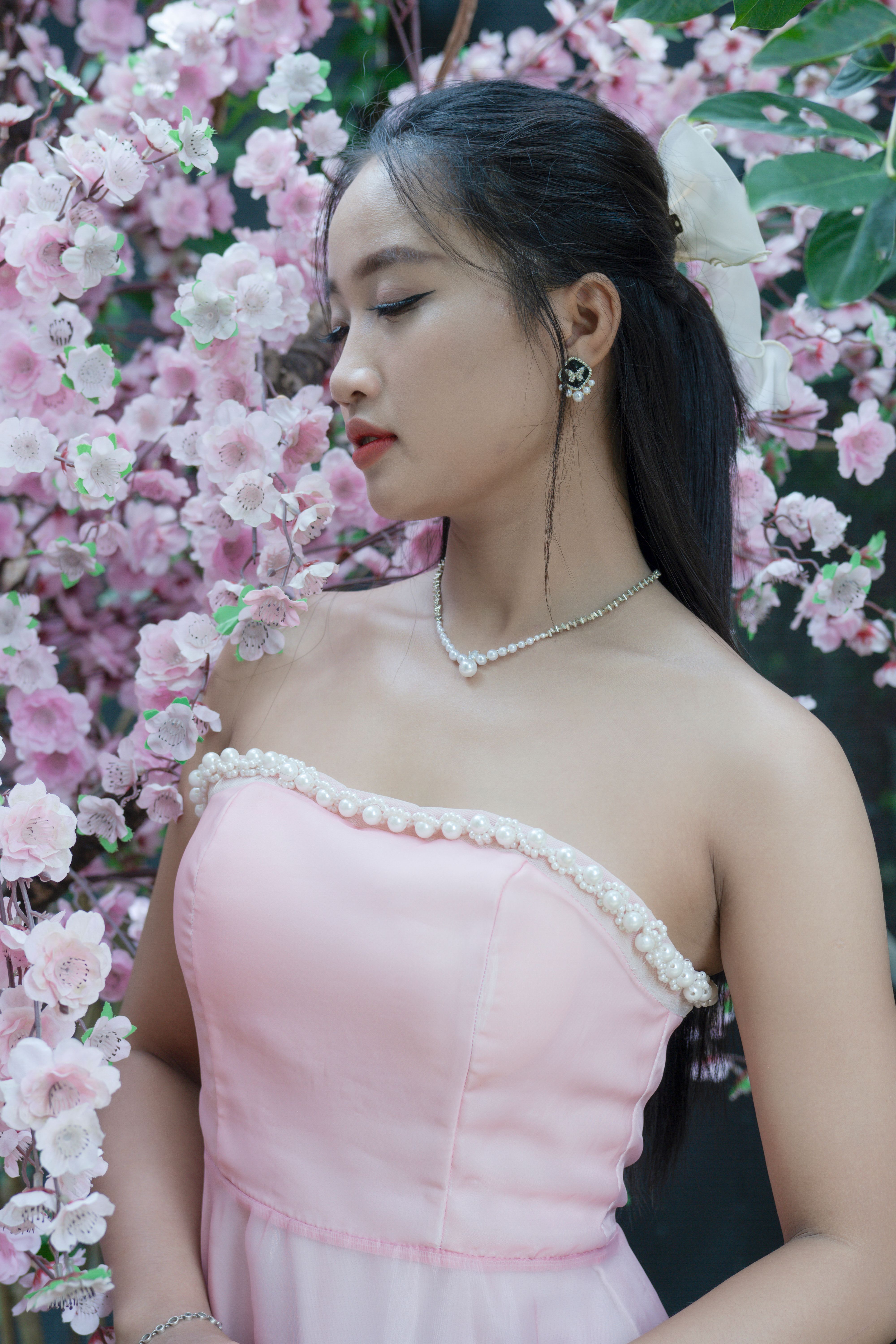 A serene portrait of a bride in a pink dress surrounded by blooming cherry blossoms, exuding elegance and beauty.