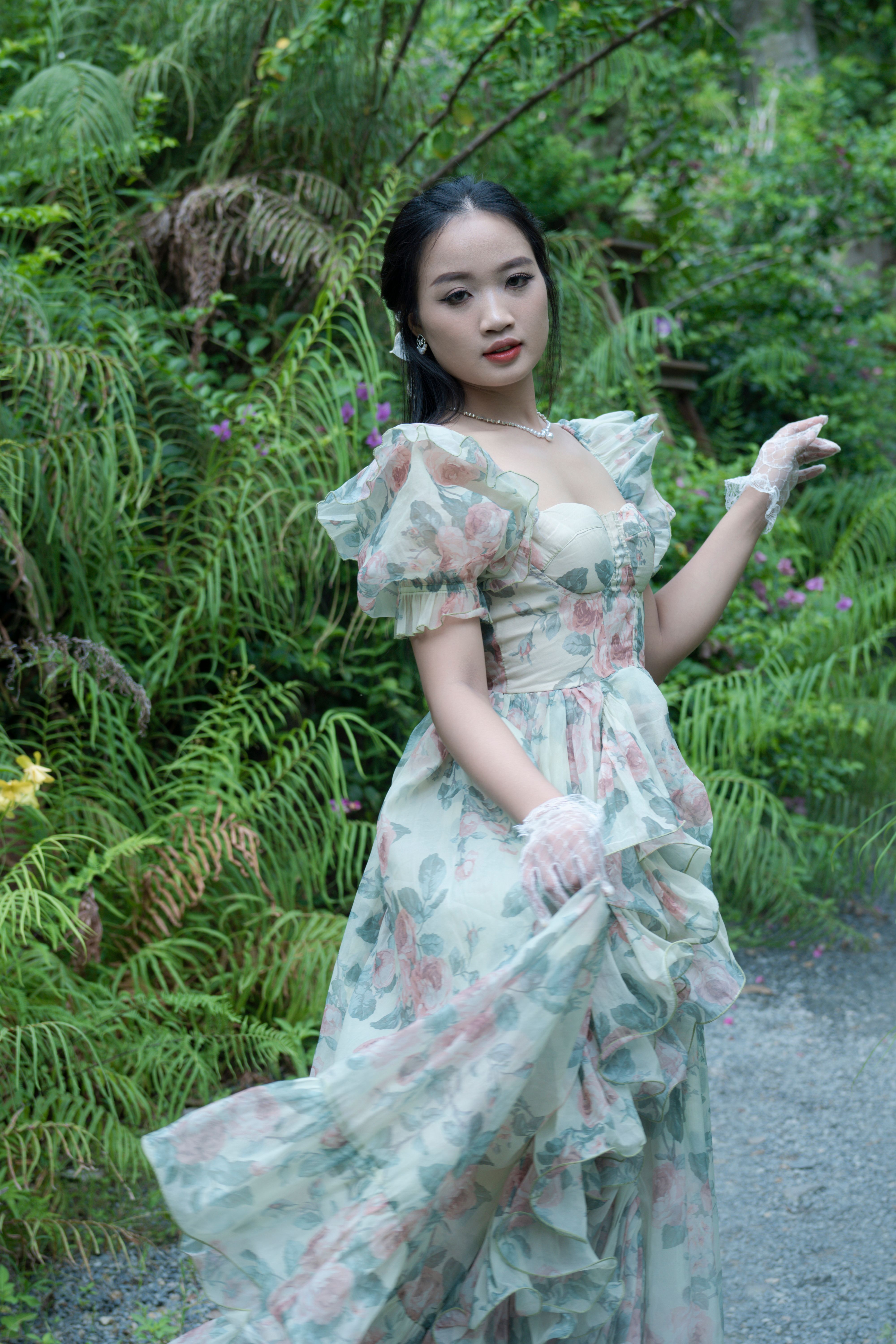 Elegant young woman in a floral dress surrounded by lush greenery in a park setting.