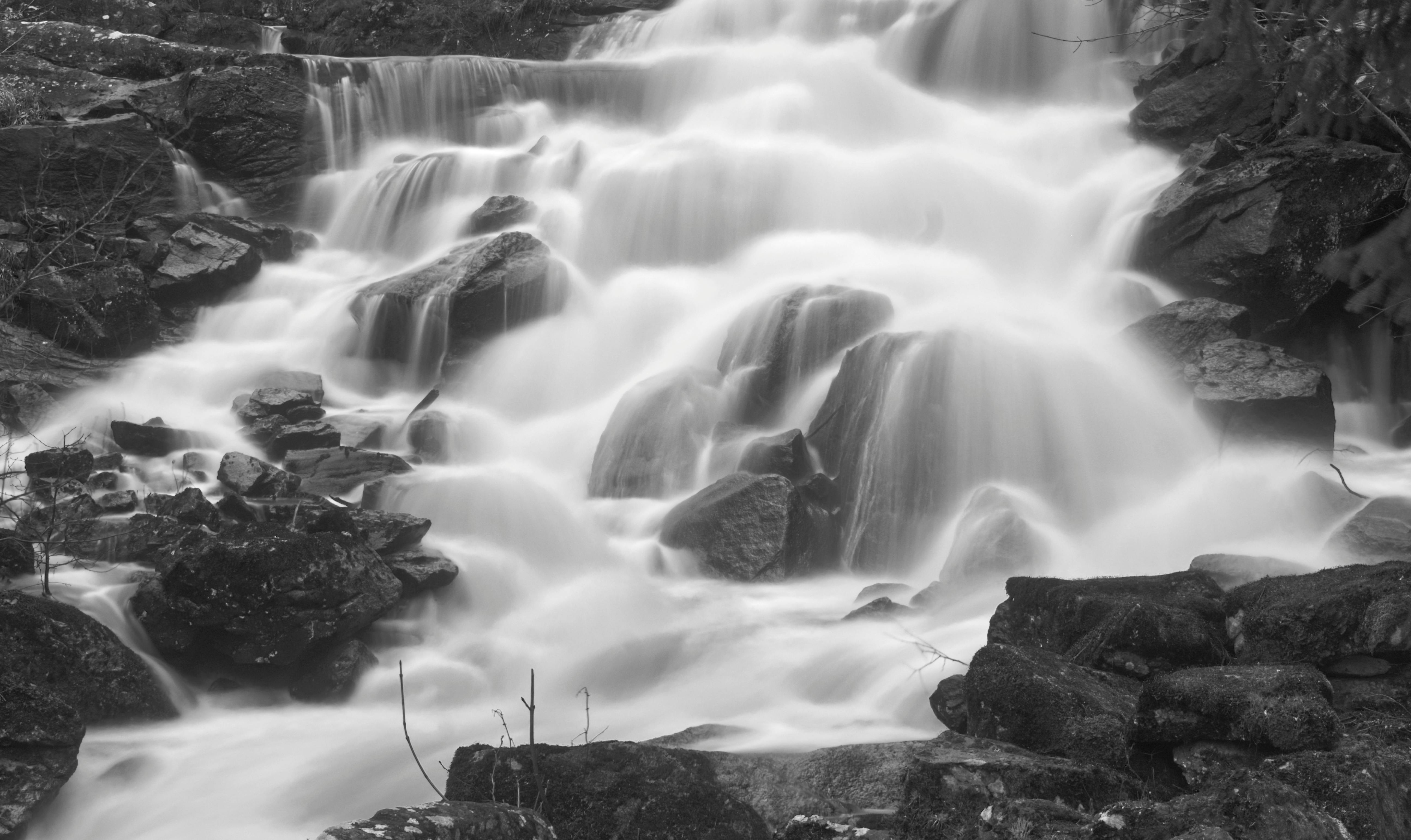 Black and white photo of a flowing waterfall over rocks in a serene forest.