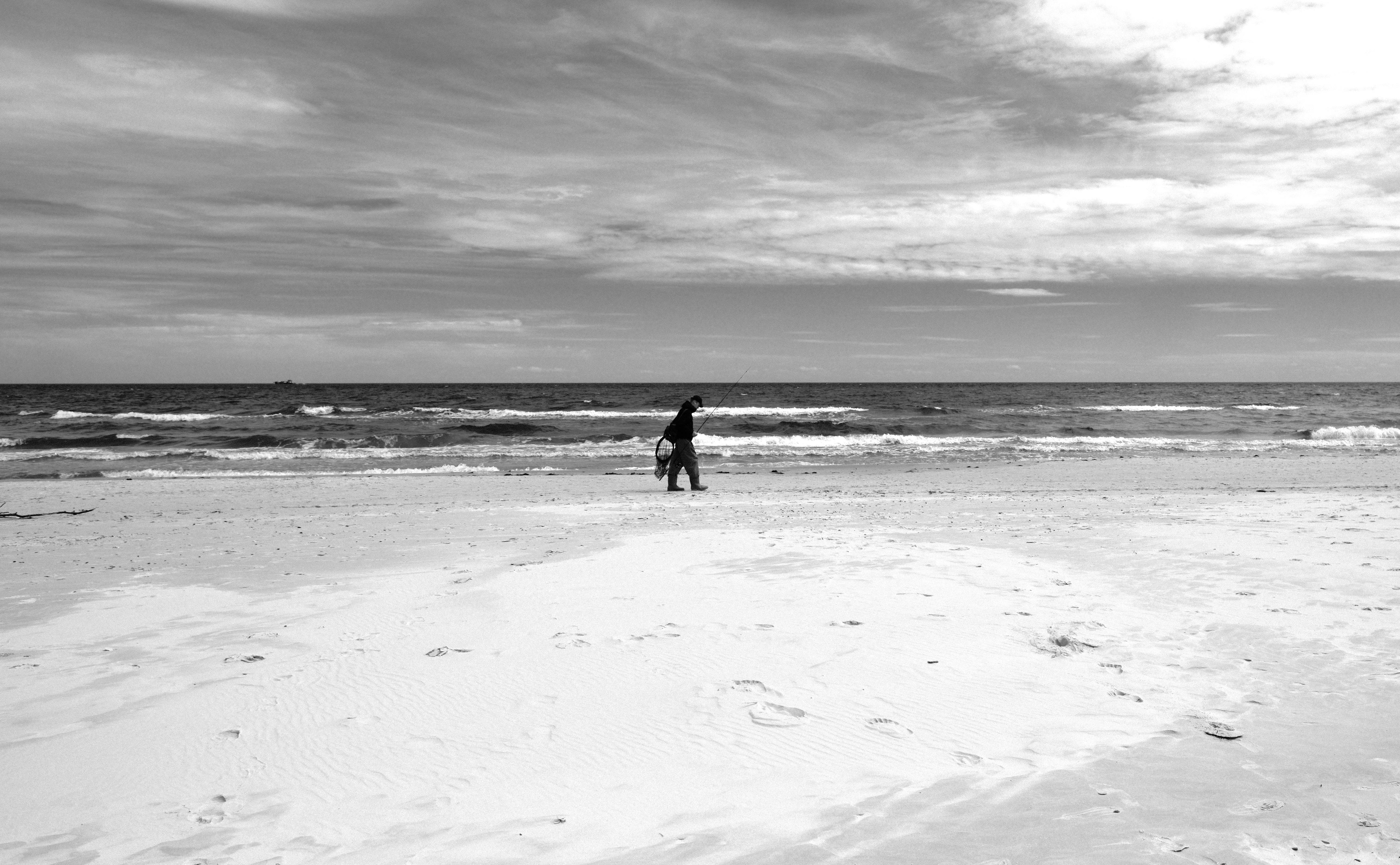 A lone figure walks along a quiet beach, captured in striking black and white.