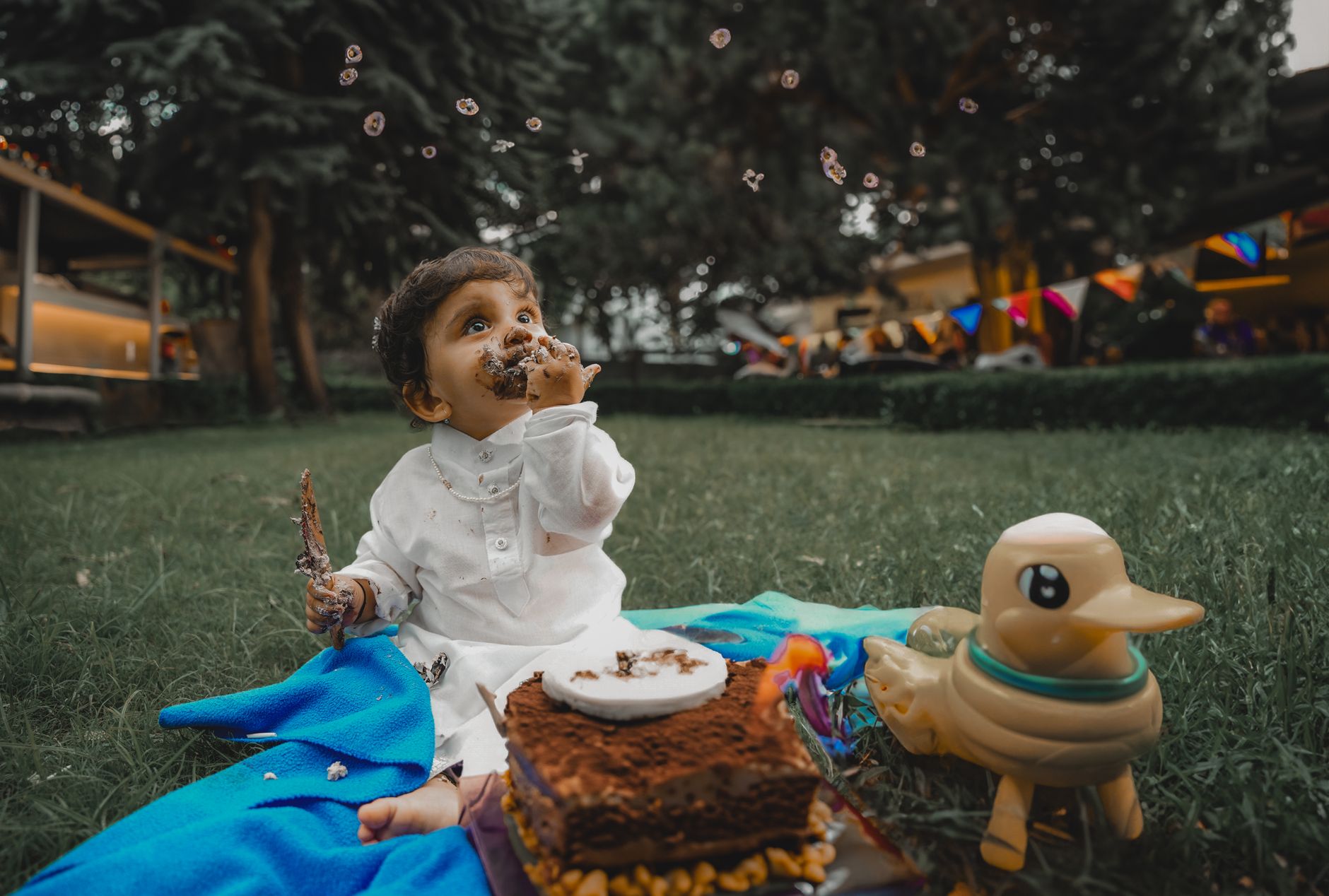Cute baby having fun with a chocolate birthday cake in a garden celebration with toys.