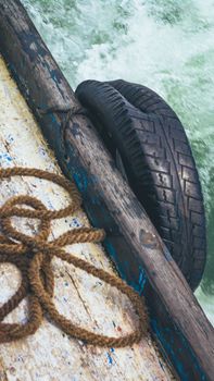 Detailed view of a rustic boat side with weathered rope and tire used as a fender on a calm sea.