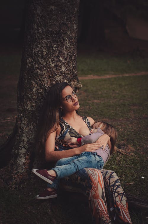 gratis Vrouw Geeft Haar Peuter Borstvoeding Onder De Boom Stockfoto