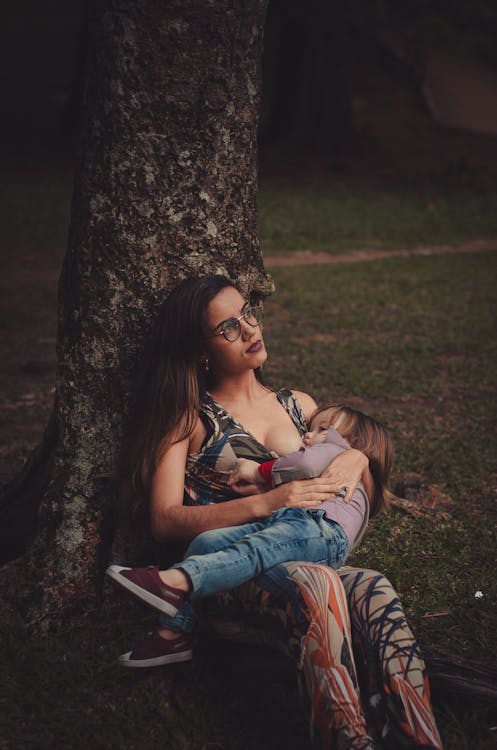 Photo of Woman Breastfeeding Her Toddler Under the Tree