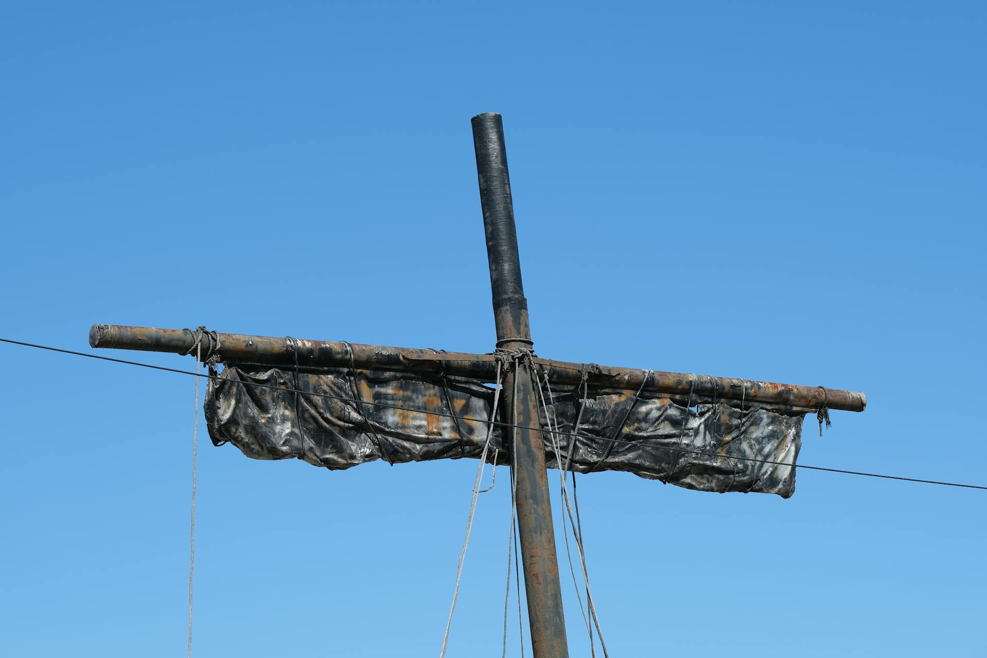 A rusty shipyard mast with ropes and weathered tarp set against a clear blue sky in İzmir.