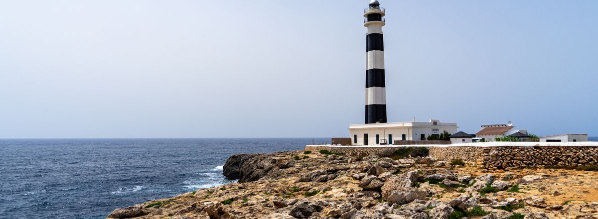 Scenic view of Cap d'Artrutx Lighthouse in Spain against a rocky coastline and expansive sea.