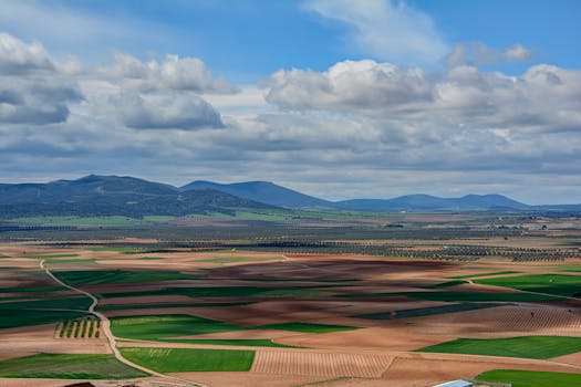 Aerial view of vast farmland and hills in Consuegra, Spain, under a cloudy sky.