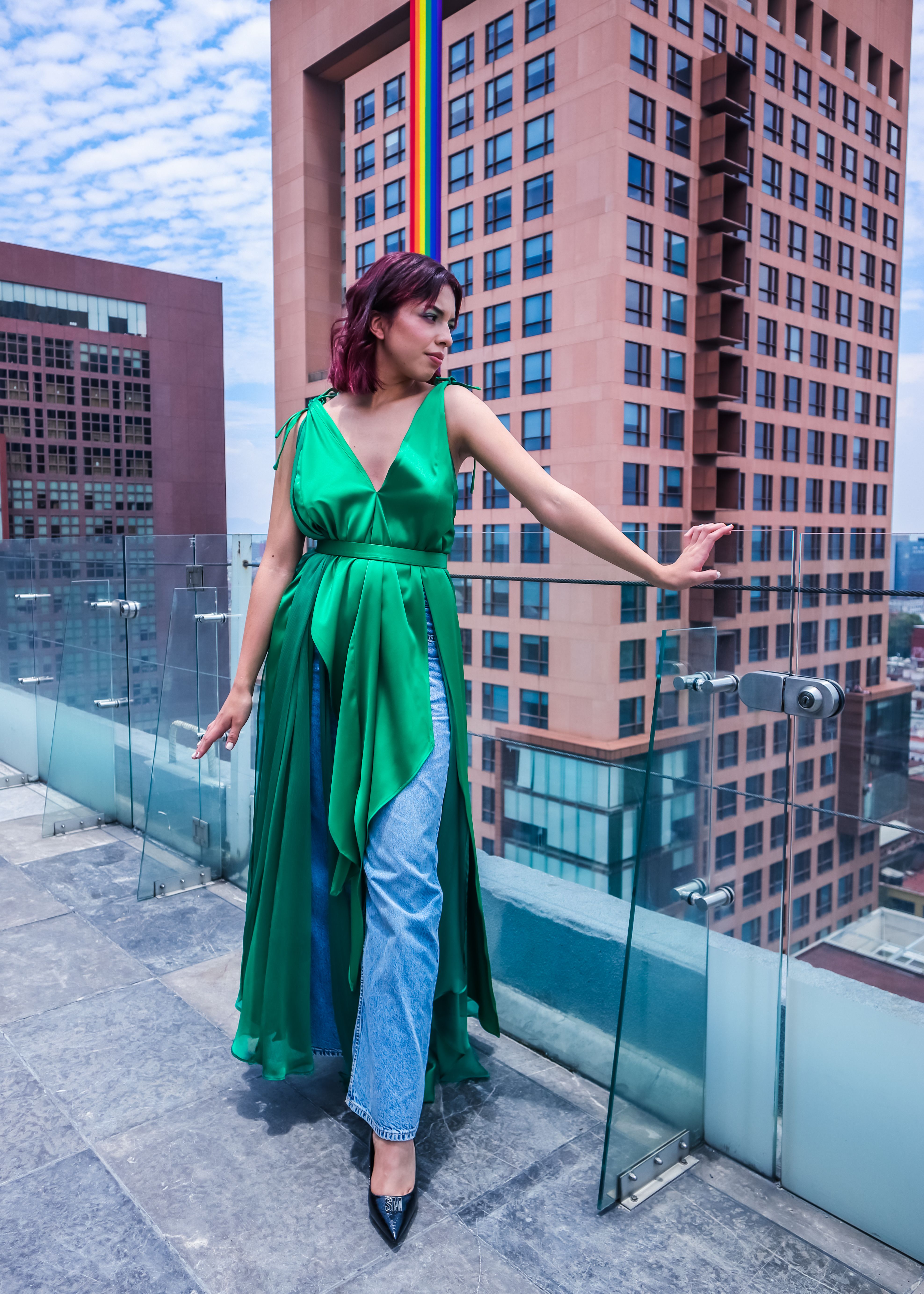 Stylish woman in green dress posing on city rooftop with skyscrapers.