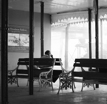 A man sits alone on a bench at the misty Darjeeling Railway Station.