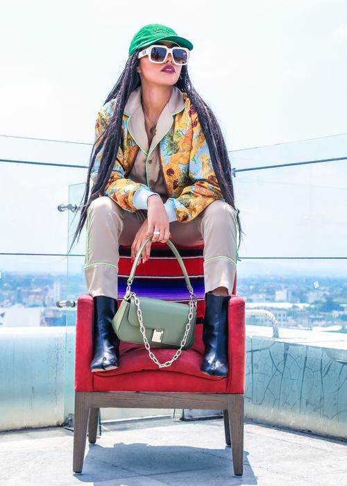 Free Fashionable woman sitting on a rooftop with sunglasses and elegant attire, showcasing a modern style. Stock Photo
