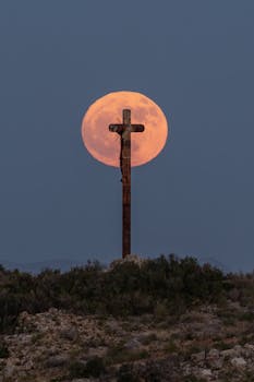 A striking cross silhouette with a glowing full moon background in Picassent, Spain.