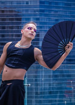 Striking portrait of a person with bold makeup holding a black fan outdoors.