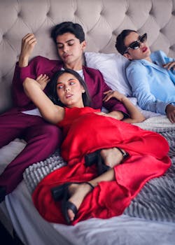 Three fashionable individuals recline in a luxurious bedroom setting, showcasing modern style and relaxation.