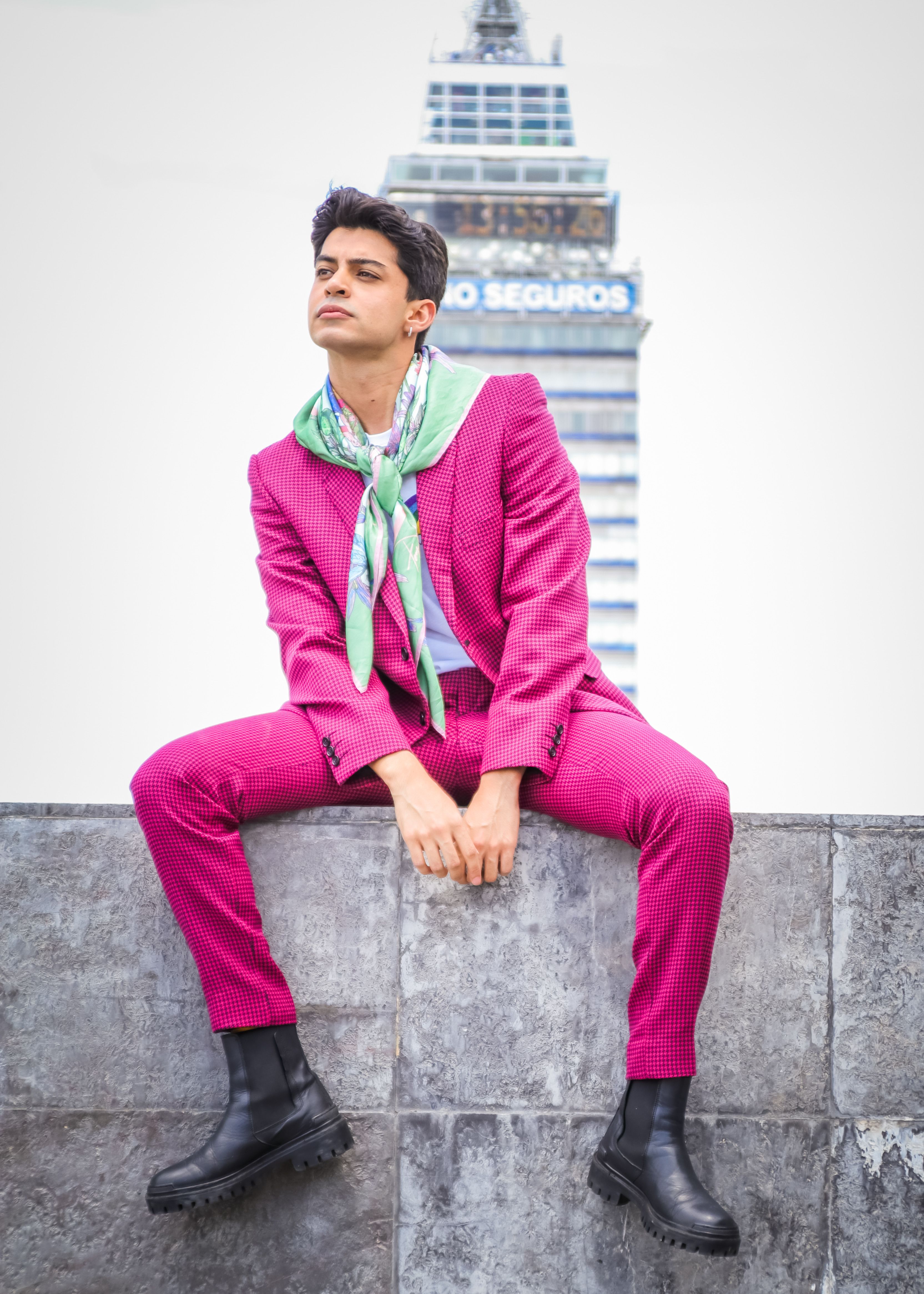 Young adult in a pink suit with a scarf poses in an urban setting. Trendy and confident.