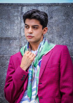 Fashionable young man posing outdoors in a pink jacket with a colorful scarf.