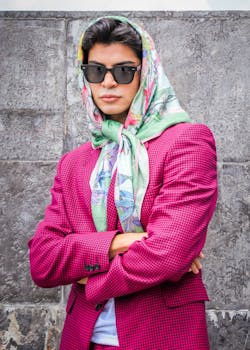 Fashionable woman wearing a vibrant pink jacket and floral scarf posing confidently outdoors.