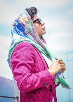 Young woman in pink blazer and colorful scarf outdoors, embodying modern fashion.