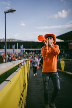 Energetic sports fan in orange blowing a horn at an outdoor stadium event.