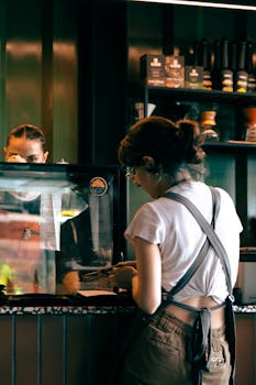 A woman orders at a trendy cafe counter, engaging with a barista. Cozy indoor ambiance.
