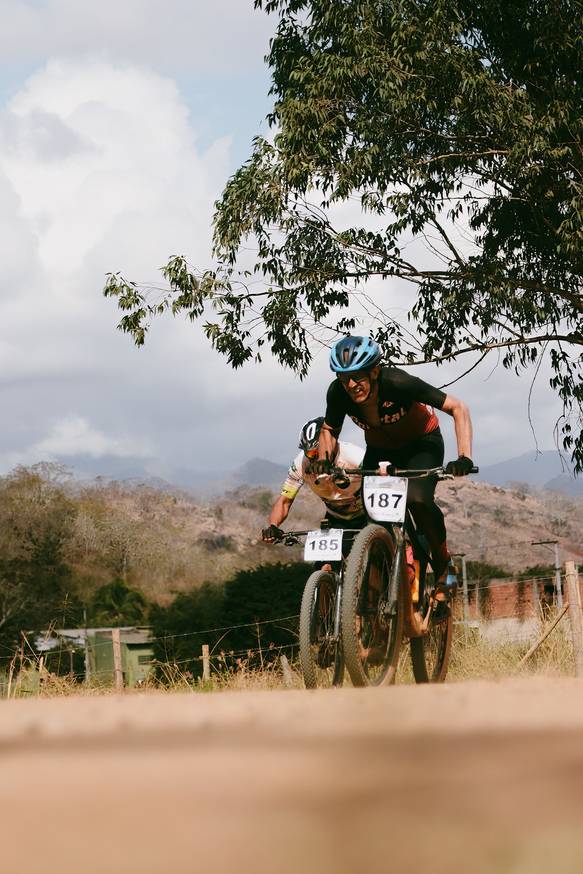 Two male cyclists racing on rugged terrain with scenic nature backdrop.