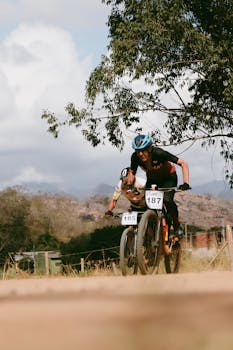 Two male cyclists racing on rugged terrain with scenic nature backdrop.