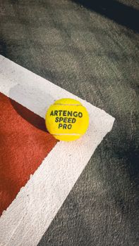 Yellow Artengo Speed Pro tennis ball on a clean outdoor court with sharp shadows.