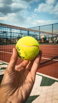Hand holding a tennis ball on an outdoor court, perfect for sports themes.