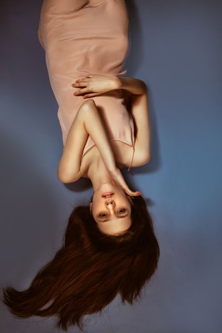Artistic portrait of a brunette woman in a pink dress lying upside down on a blue background.