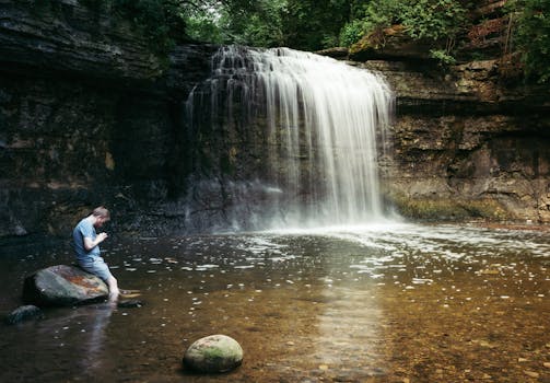 A person stands by a peaceful waterfall in a forest setting, capturing a moment of reflection.