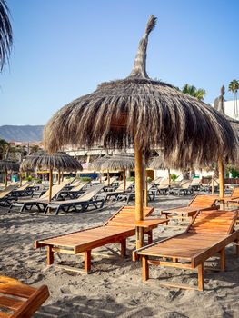 Relaxing beach scene with wooden loungers and straw umbrellas at Costa Adeje, Spain.