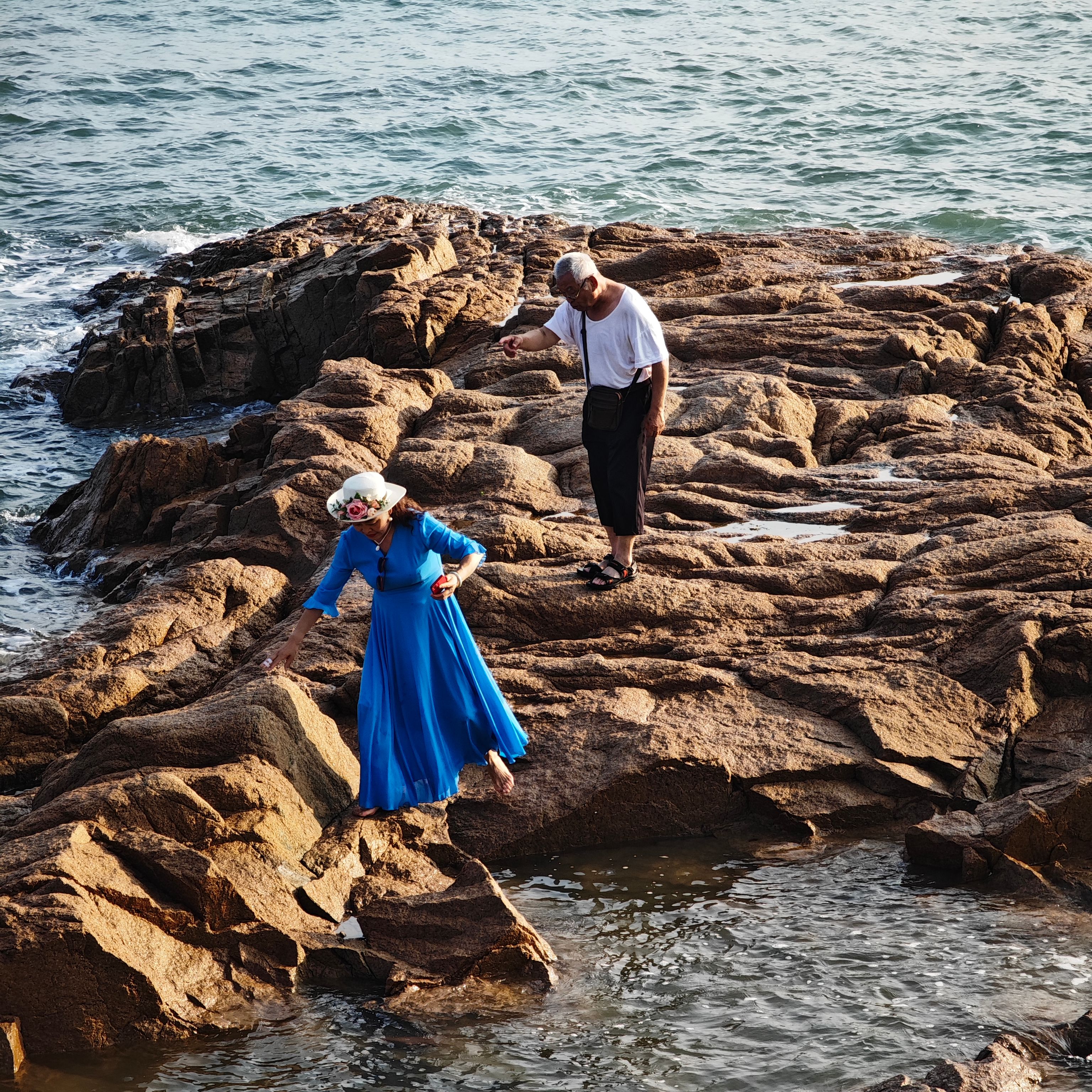 Two adults venturing across a rocky seaside landscape in warm summer weather.