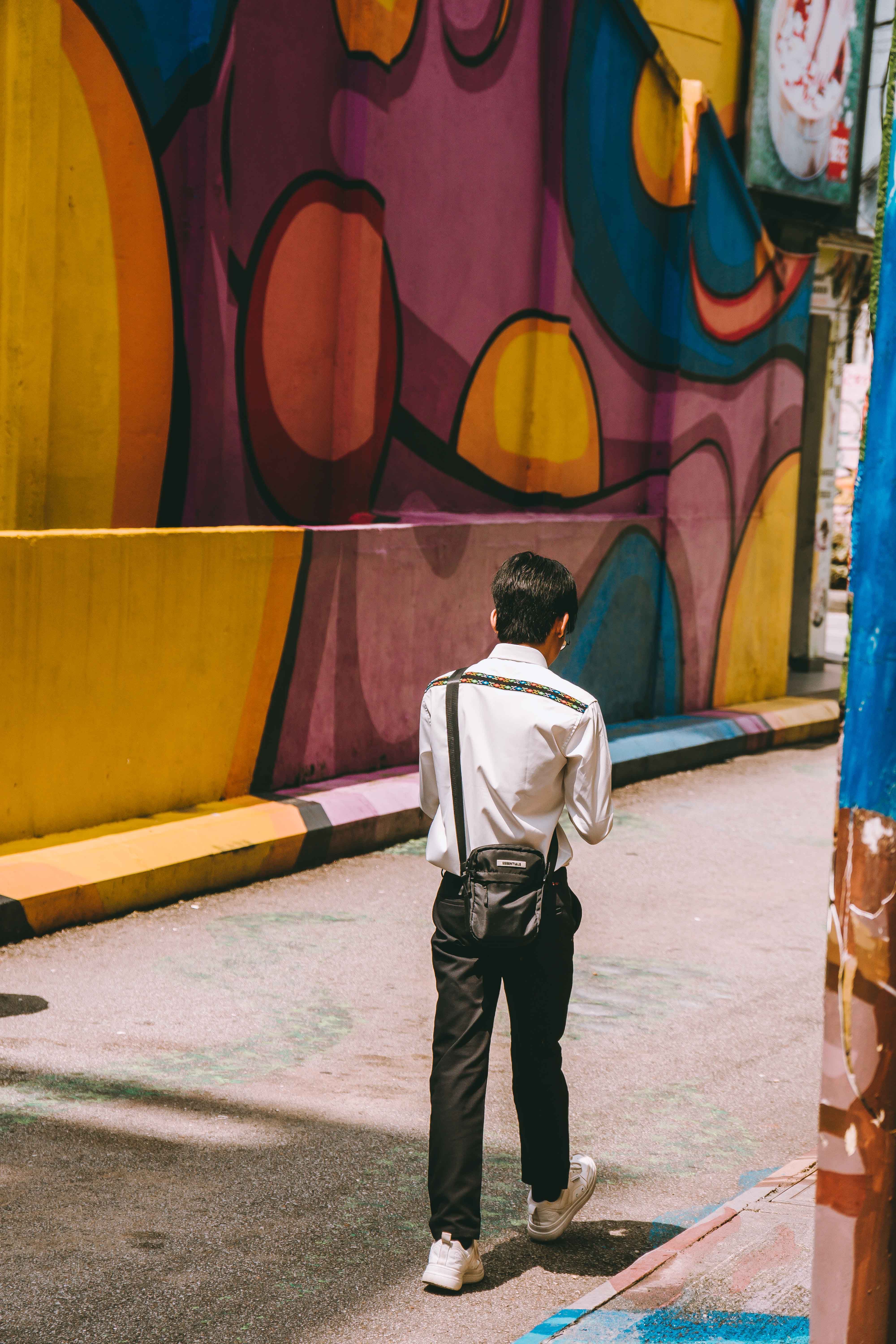 A man walking down a street with graffiti on the wall