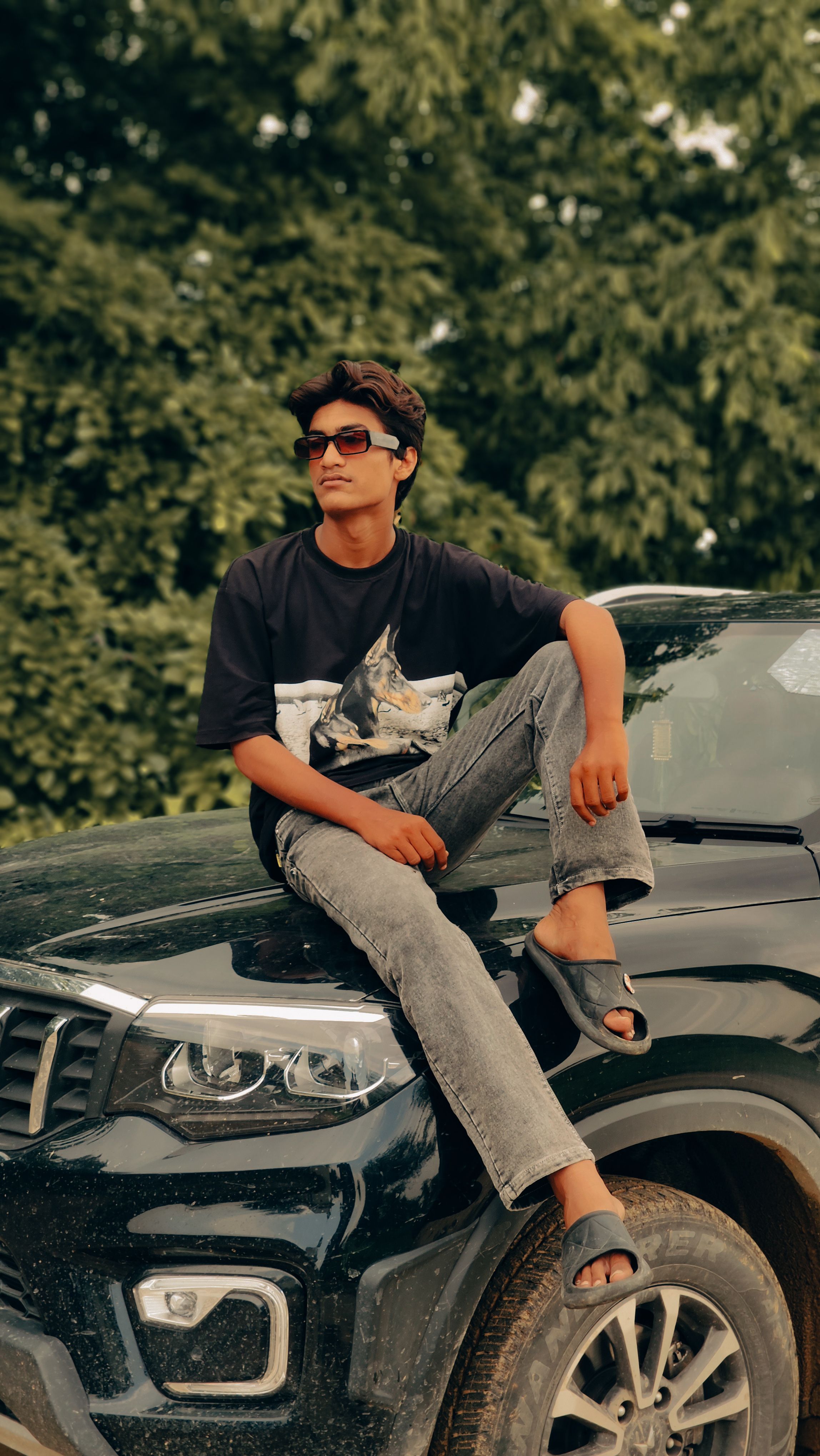 Teenage boy sitting on a car hood, enjoying leisure time outdoors in India.