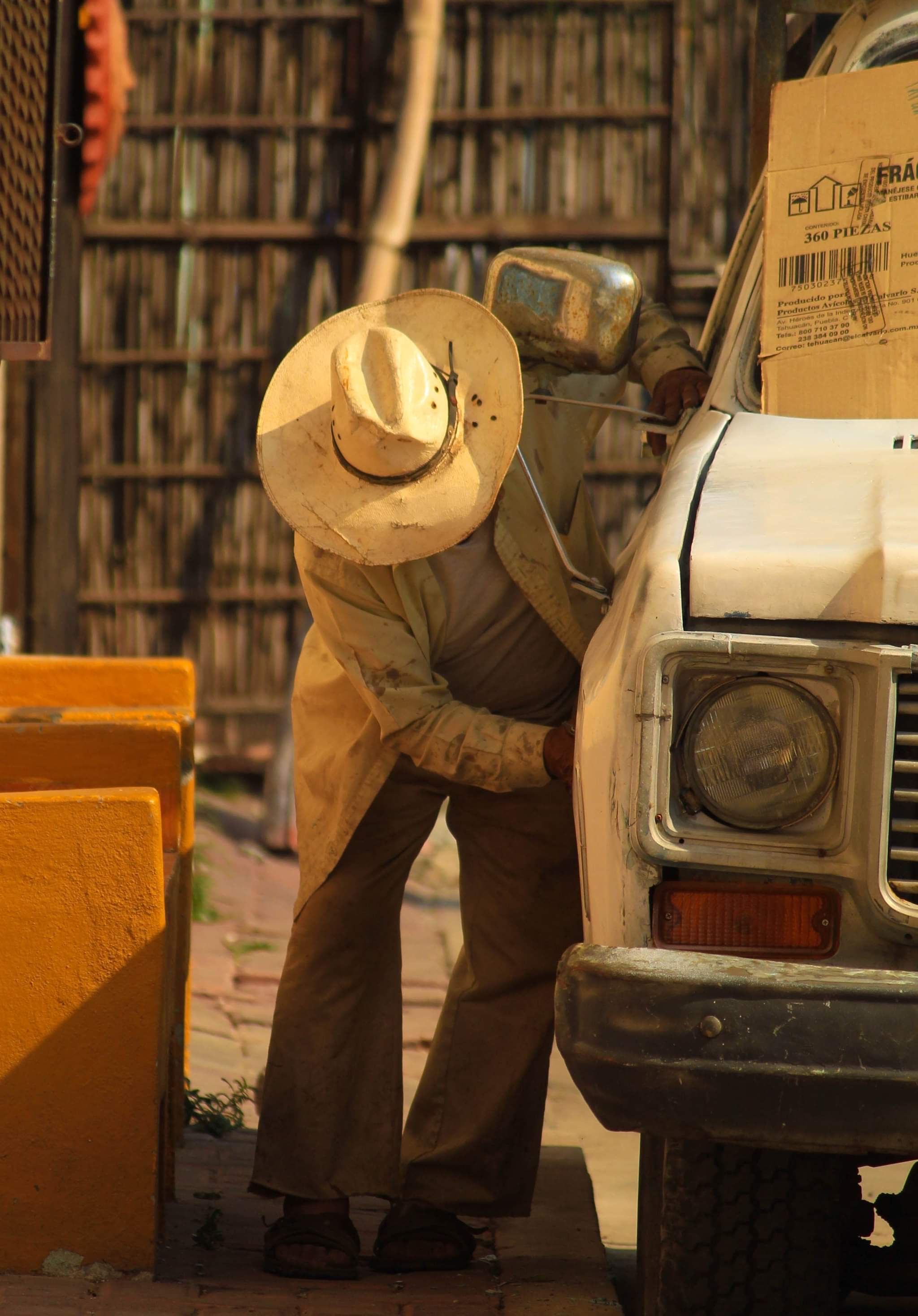 A man in rustic attire checks a pickup truck outdoors, embodying manual labor.
