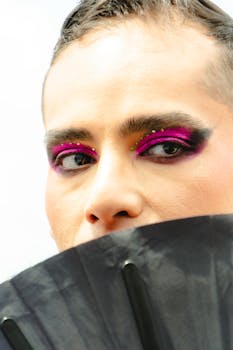 Striking portrait of a person with vibrant eye makeup partially obscured by a black hand fan.