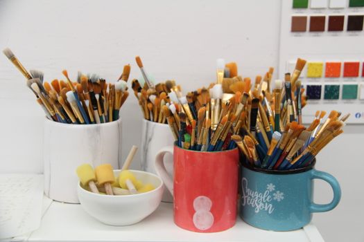 Colorful assortment of paintbrushes neatly arranged in ceramic mugs for an artistic workspace.