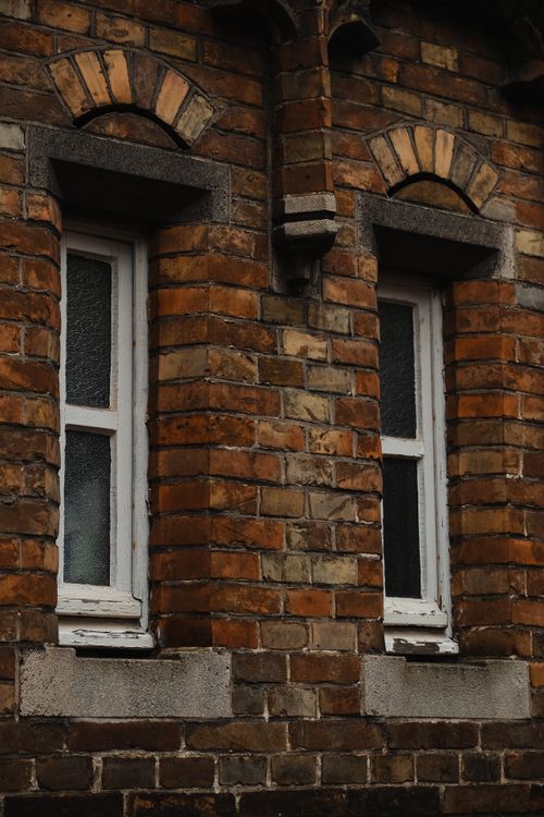 Free Detailed view of an antique brick wall facade featuring two vintage windows. Stock Photo