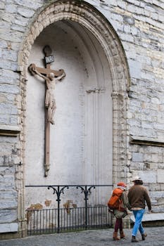 A couple walks past a historical church facade with a prominent crucifix.