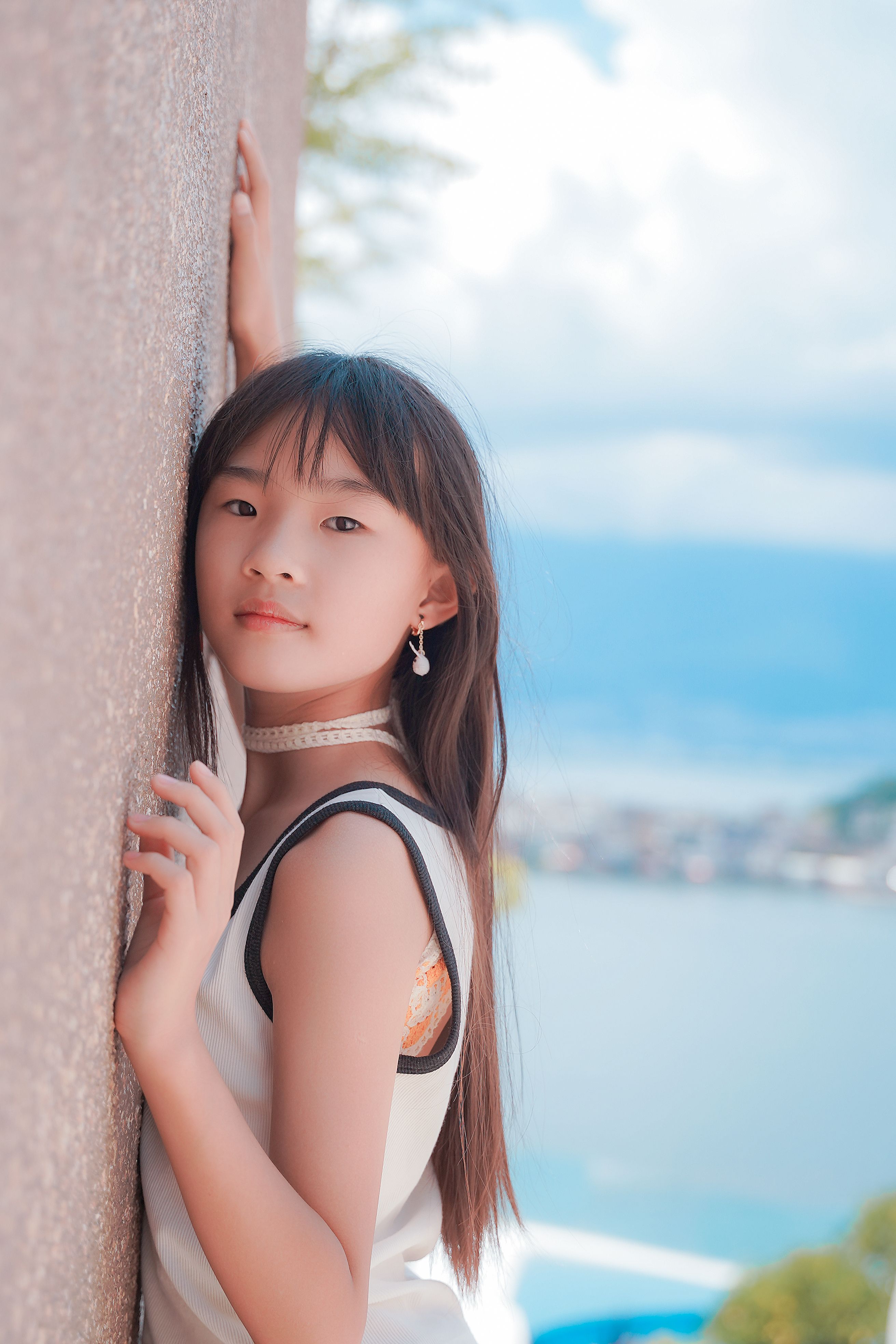 Young girl posing by a wall with a scenic backdrop, embodying a relaxed summer vibe.