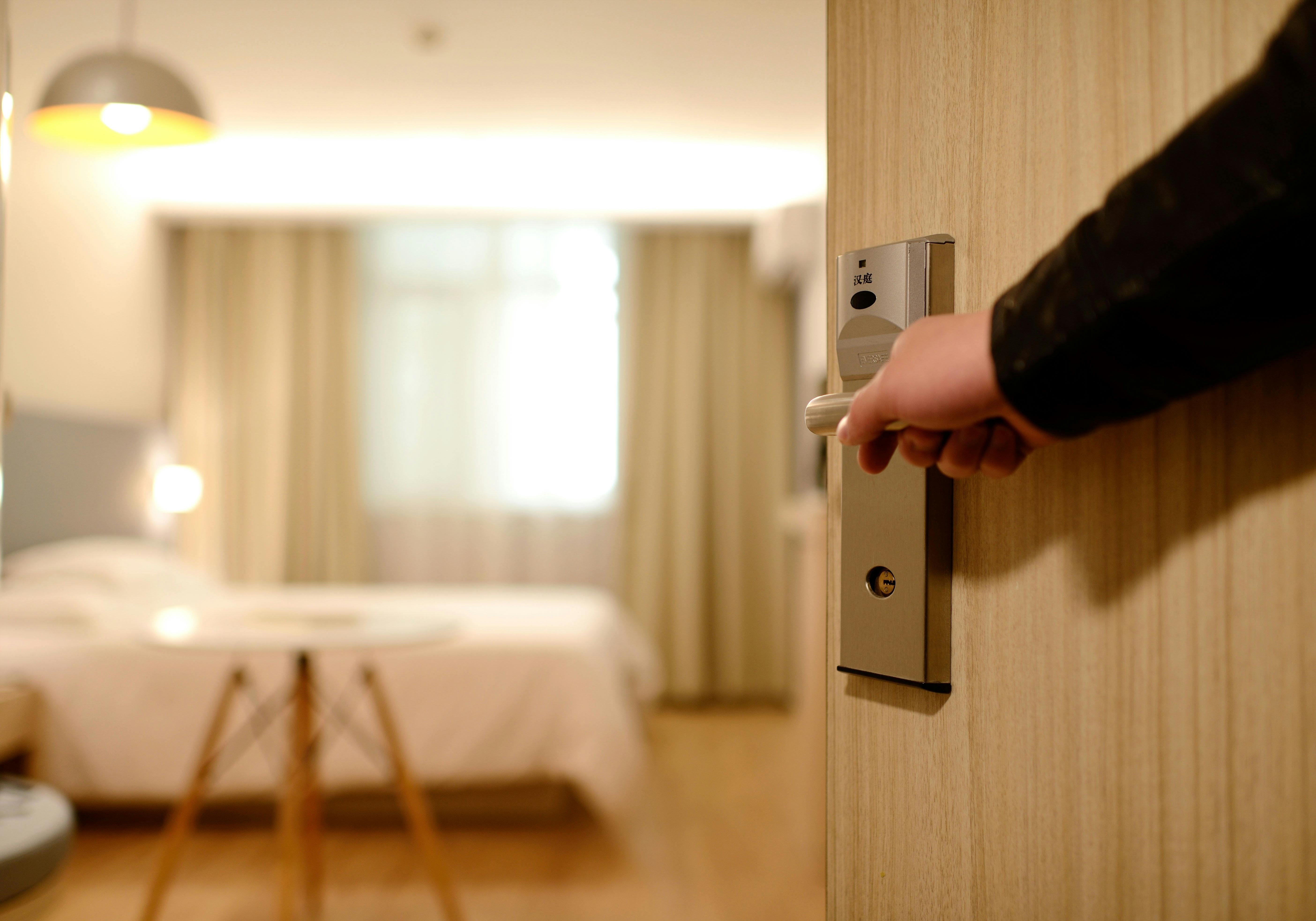 Hand opening hotel room door, representing arrival and the start of privacy protection checks.