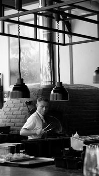 A chef working in a stylish kitchen with a brick oven and pendant lights.
