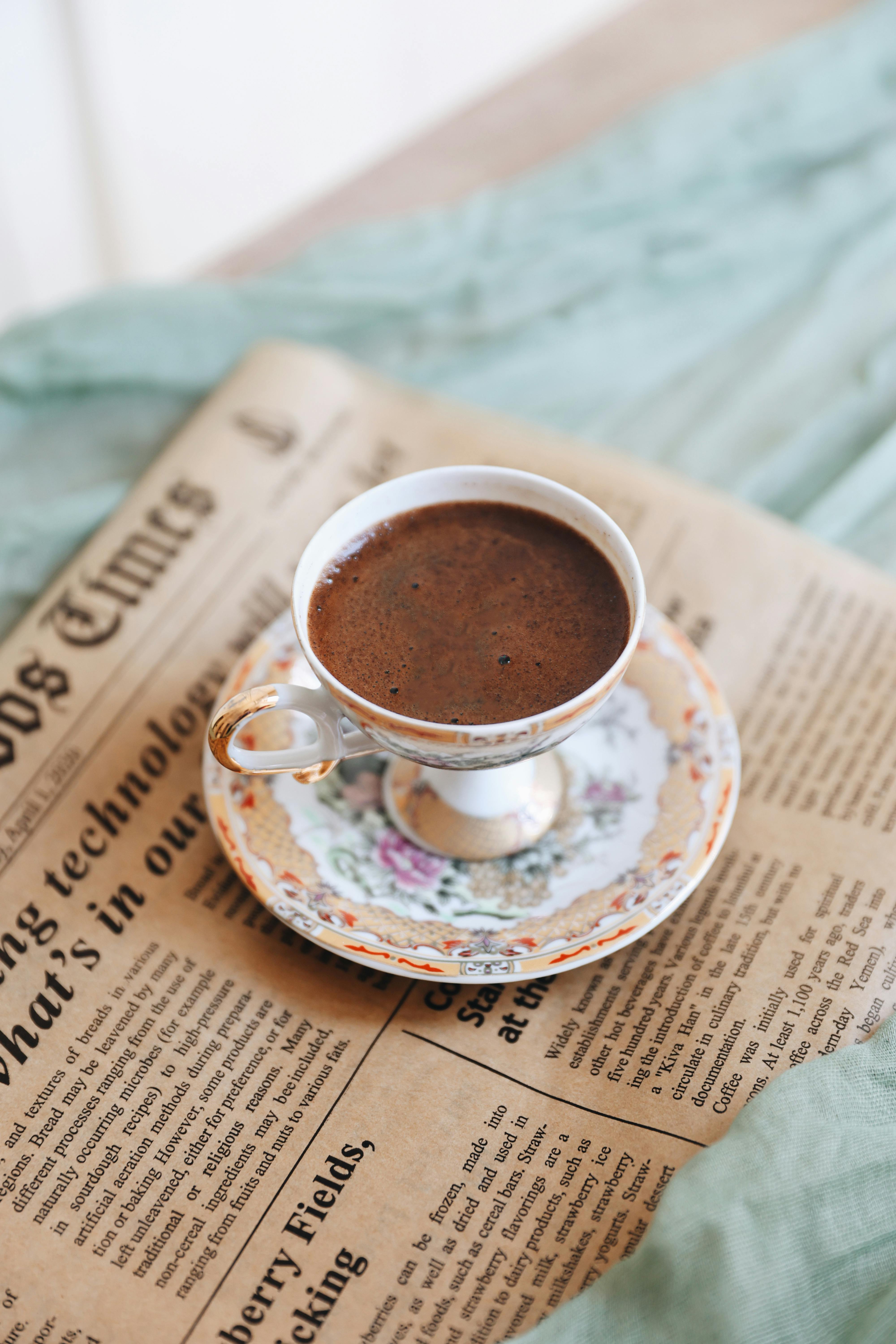 A floral porcelain coffee cup rests on a vintage newspaper, exuding classic charm.
