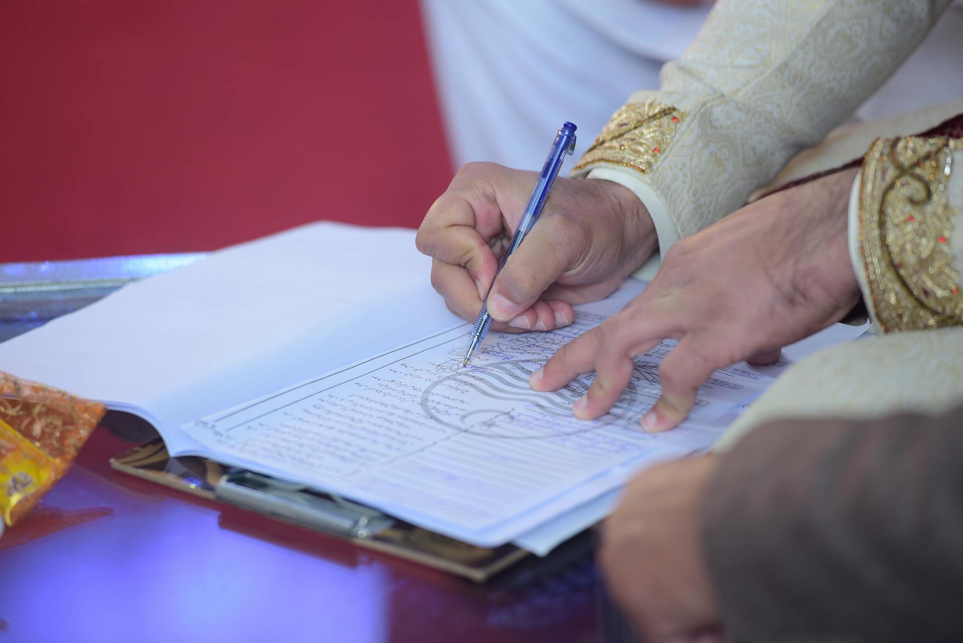 Close-up of a groom signing the marriage contract during a traditional Pakistani wedding ceremony.