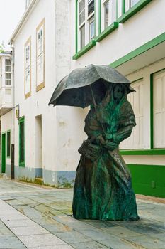 Bronze statue of a woman with umbrella in the streets of Ortigueira, Spain. Urban art and architecture.