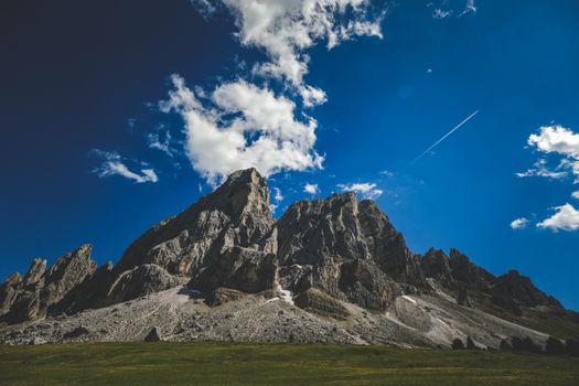 Scenic view of sharp rocky mountain peaks under a vibrant blue sky with fluffy clouds.
