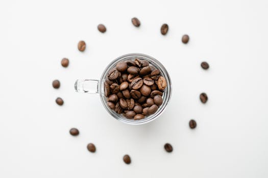 Artistic top shot of coffee beans in a glass mug, arranged in a circle on a white surface.