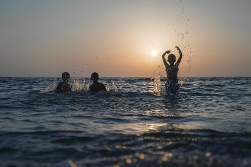 Free Silhouettes of children enjoying playful moments in ocean waters during sunset. Stock Photo