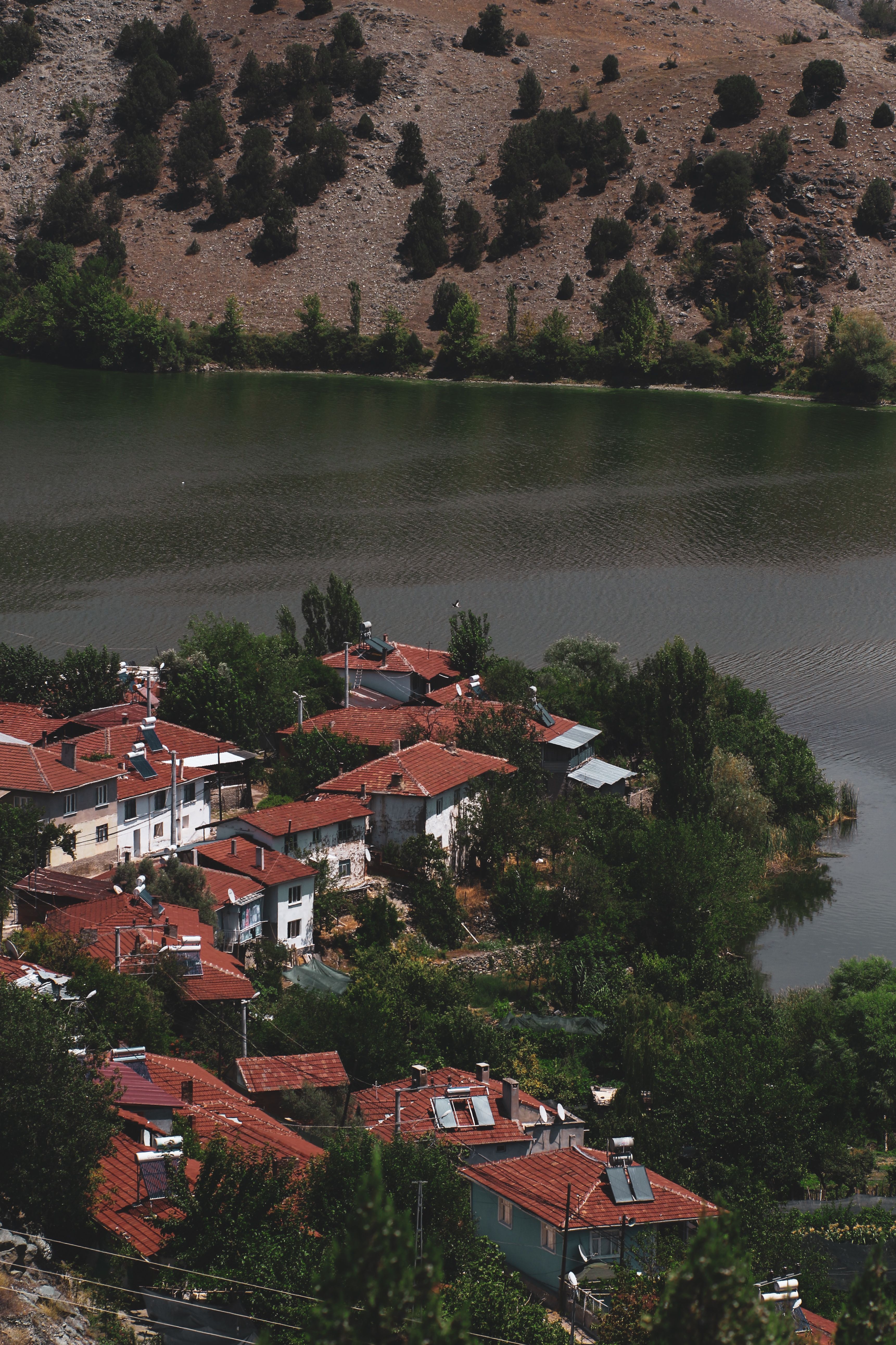 A picturesque, serene village with red roofs by a tranquil lake and lush hillside landscape.