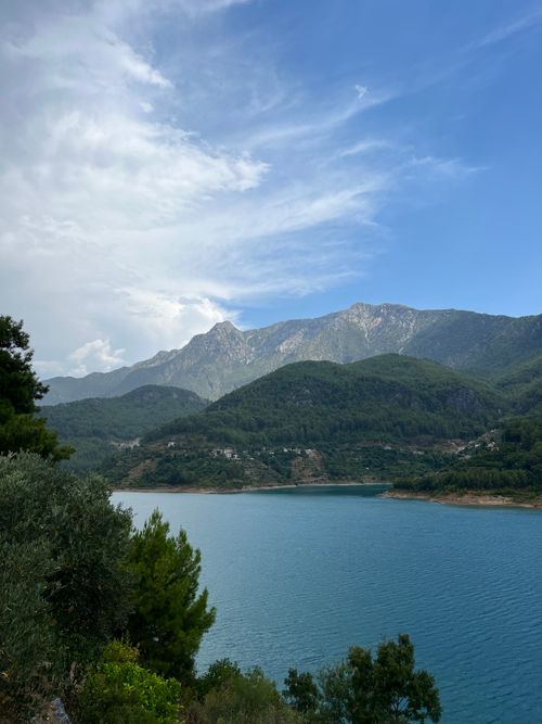 Free Explore the tranquil beauty of a serene mountain lake surrounded by lush green hills under a vibrant blue sky. Stock Photo