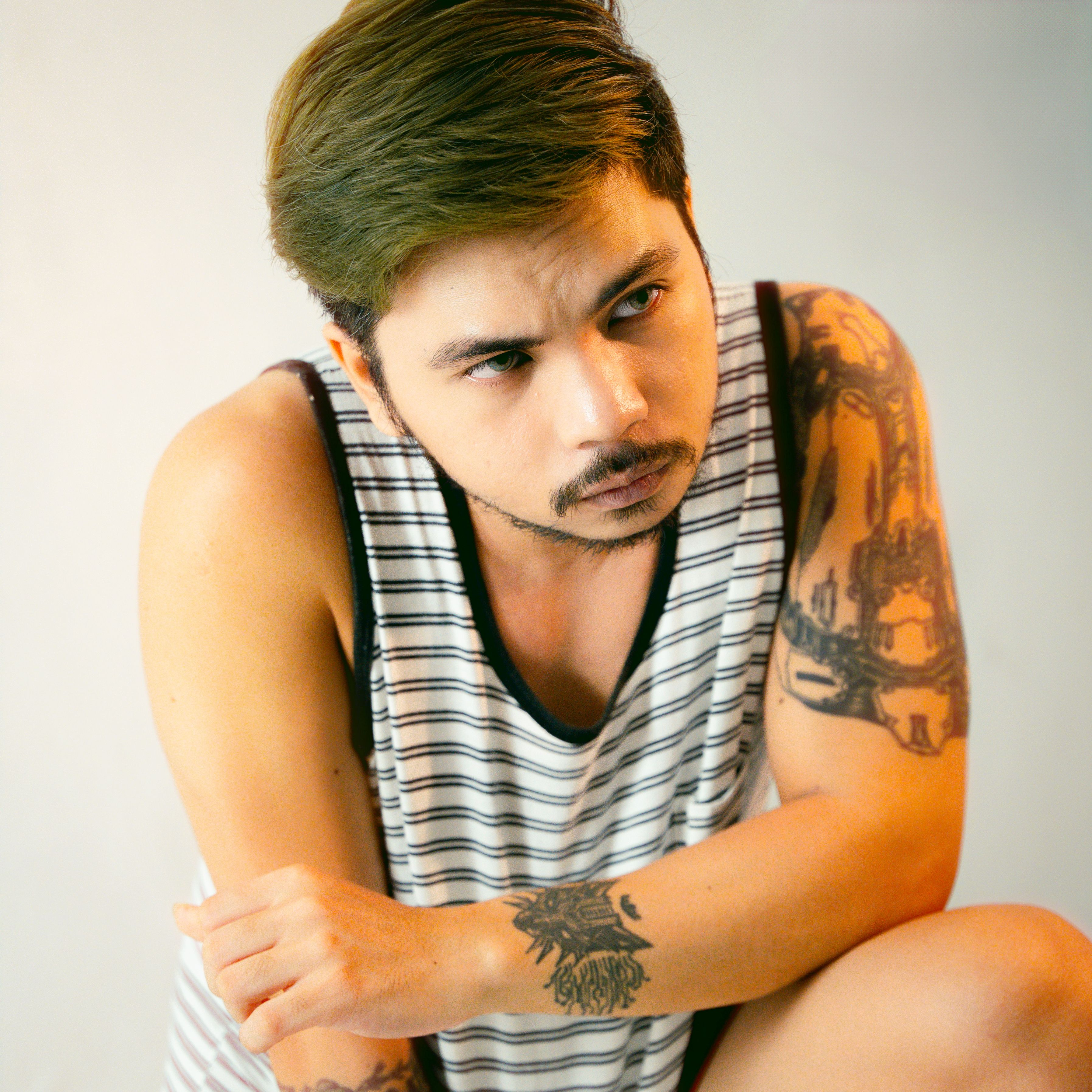 Portrait of a stylish man with tattoos in a striped tank top, exuding a cool attitude.